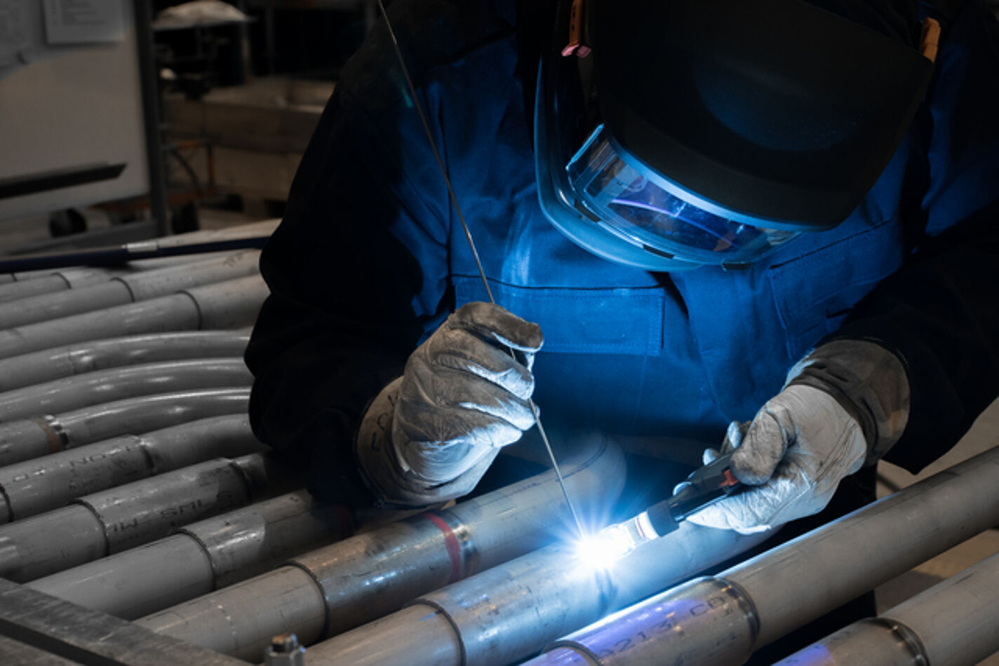 Lasser in beschermende kleding legt een TIG las op stalen buizen in een industriële omgeving
